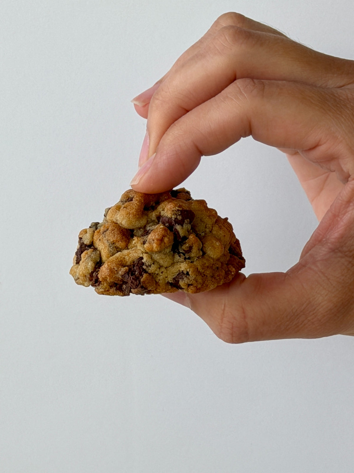 Side view of a thick Chocolate Chip NYC Mini cookie held by Big Sweet Tasty